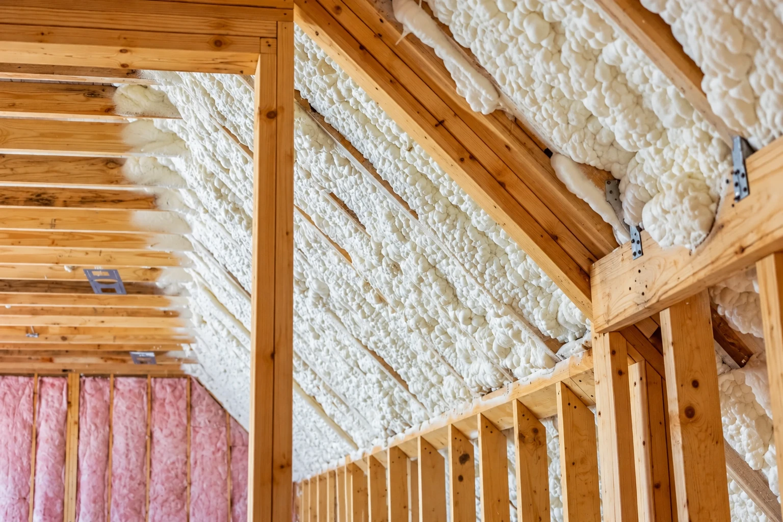 White spray foam seals the sloped roof framing in an unfinished attic.