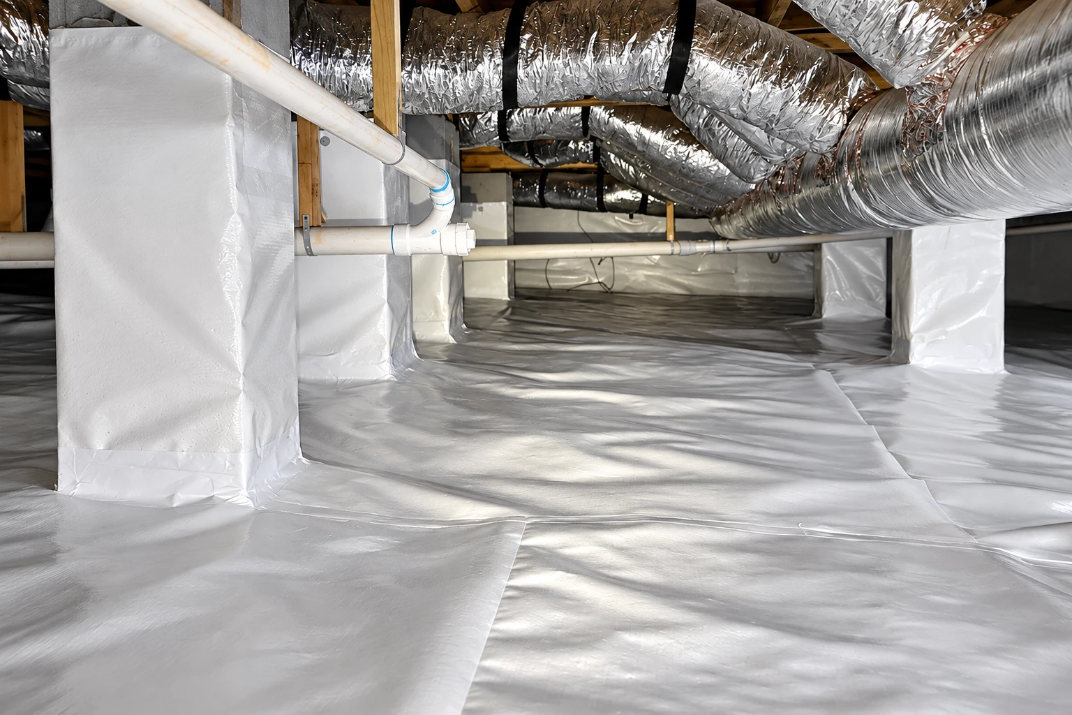 Crawl space with a white vapor barrier covering the floor and support piers beneath silver HVAC ducts.
