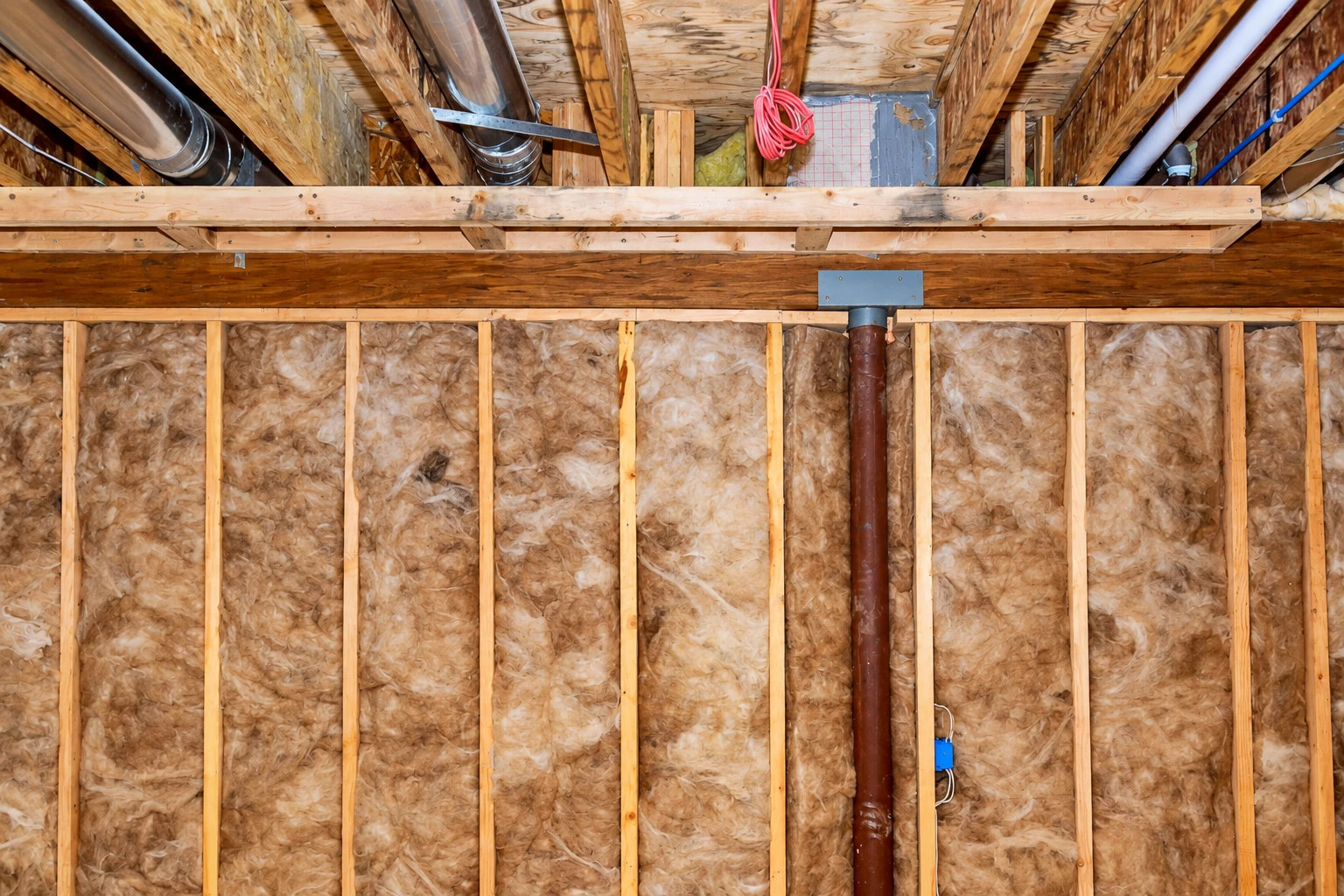 Fiberglass insulation fills the wall cavities of an unfinished home beneath exposed joists and ductwork.