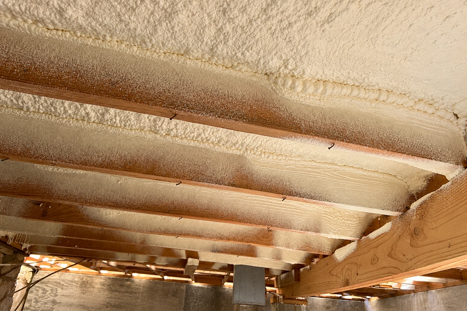 Cream-colored spray foam covers the underside of roof decking between exposed wooden rafters.